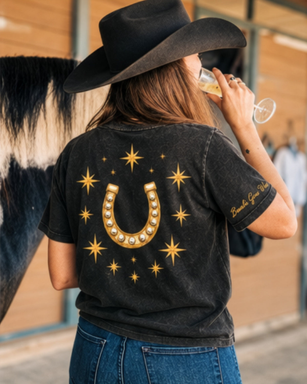 Icon Tee in black, back, worn with a black hat beside a paint horse.